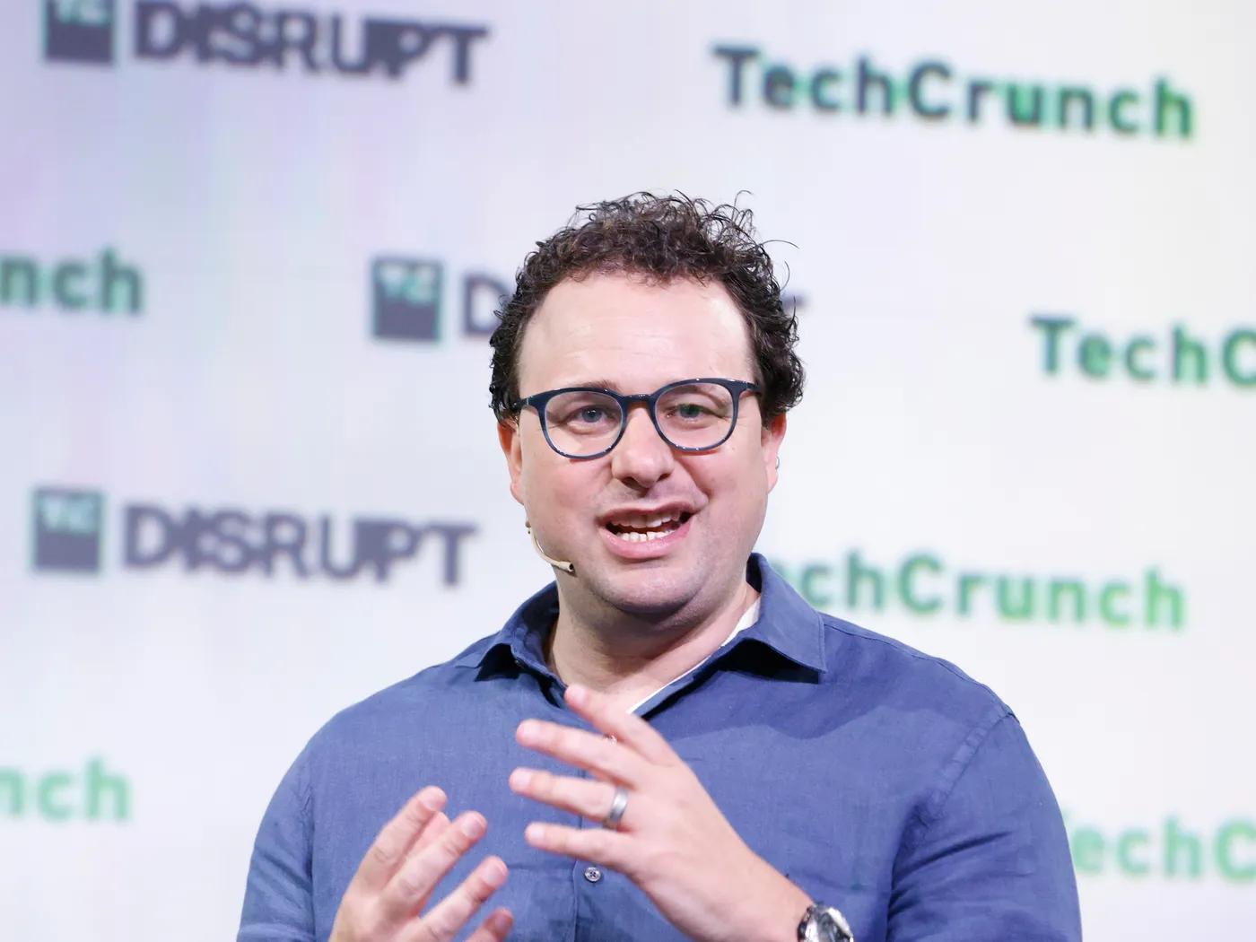 Dario Amodei, lunettes et chemise bleue, parle sur scène devant le décor TechCrunch Disrupt